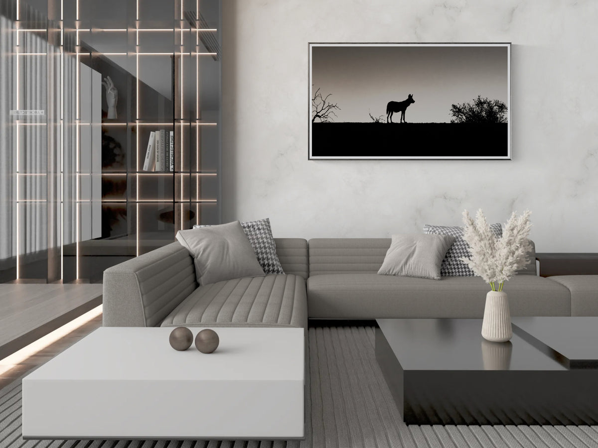 A modern living room featuring a grey sectional sofa, a white coffee table, and a framed black and white landscape fine art print of a silhouetted African wild dog.