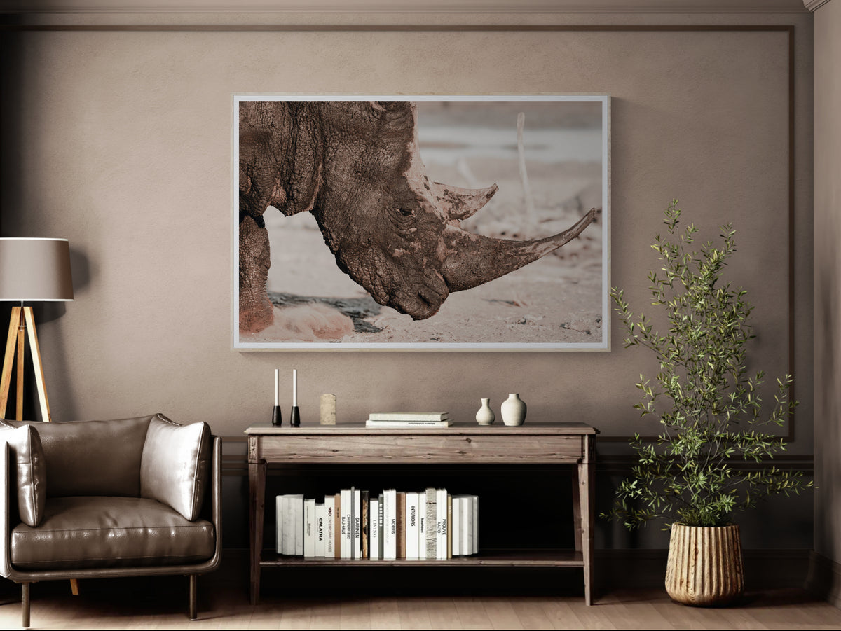 A framed wall art print depicting a close-up rhinoceros head in muted earth tones, displayed above a wooden console table in a styled living room.