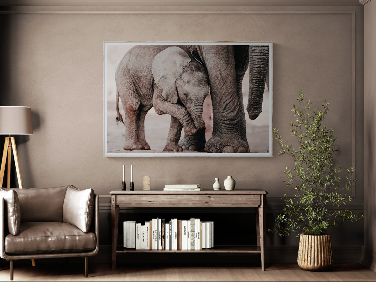 A large framed wall art print depicting a close-up photograph of an elephant and baby elephant, displayed in a modern living room setting above a wooden console table.